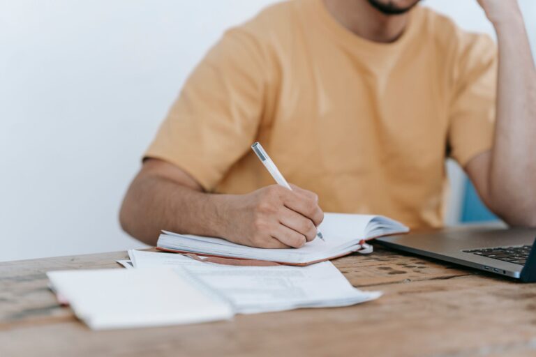 Person taking notes beside a laptop while working through a guide
